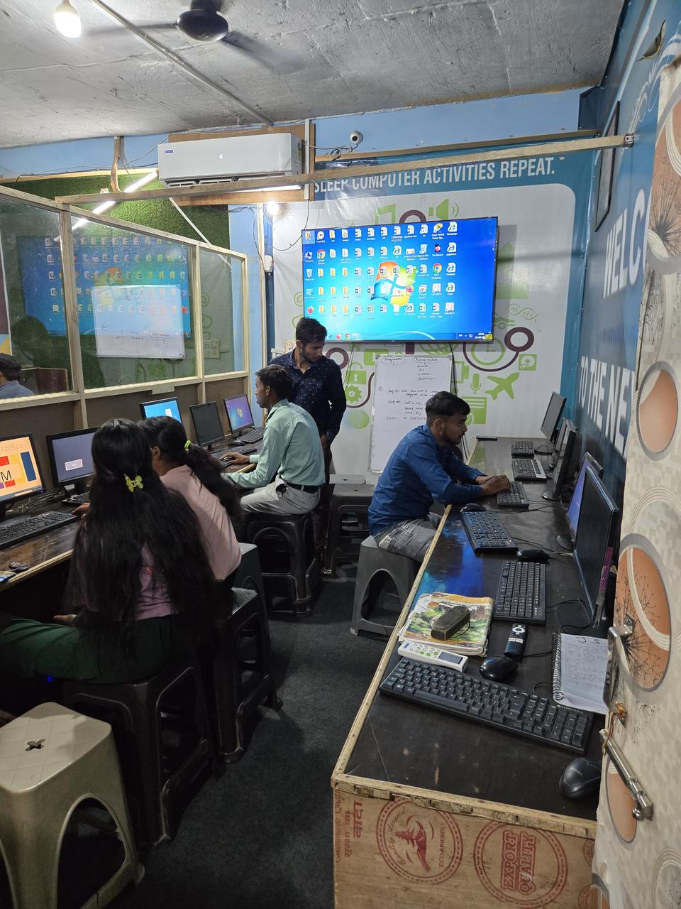 Students practising on computers in the VidyaTech lab while a lesson is shown on a large wall-mounted screen